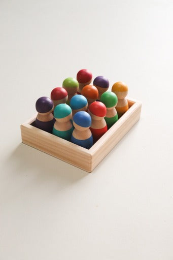 A set of colorful wooden peg dolls placed in a wooden tray, with no facial features painted on the dolls.