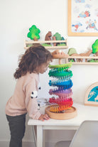Child dropping a wooden marble into the top of the rainbow marble tower