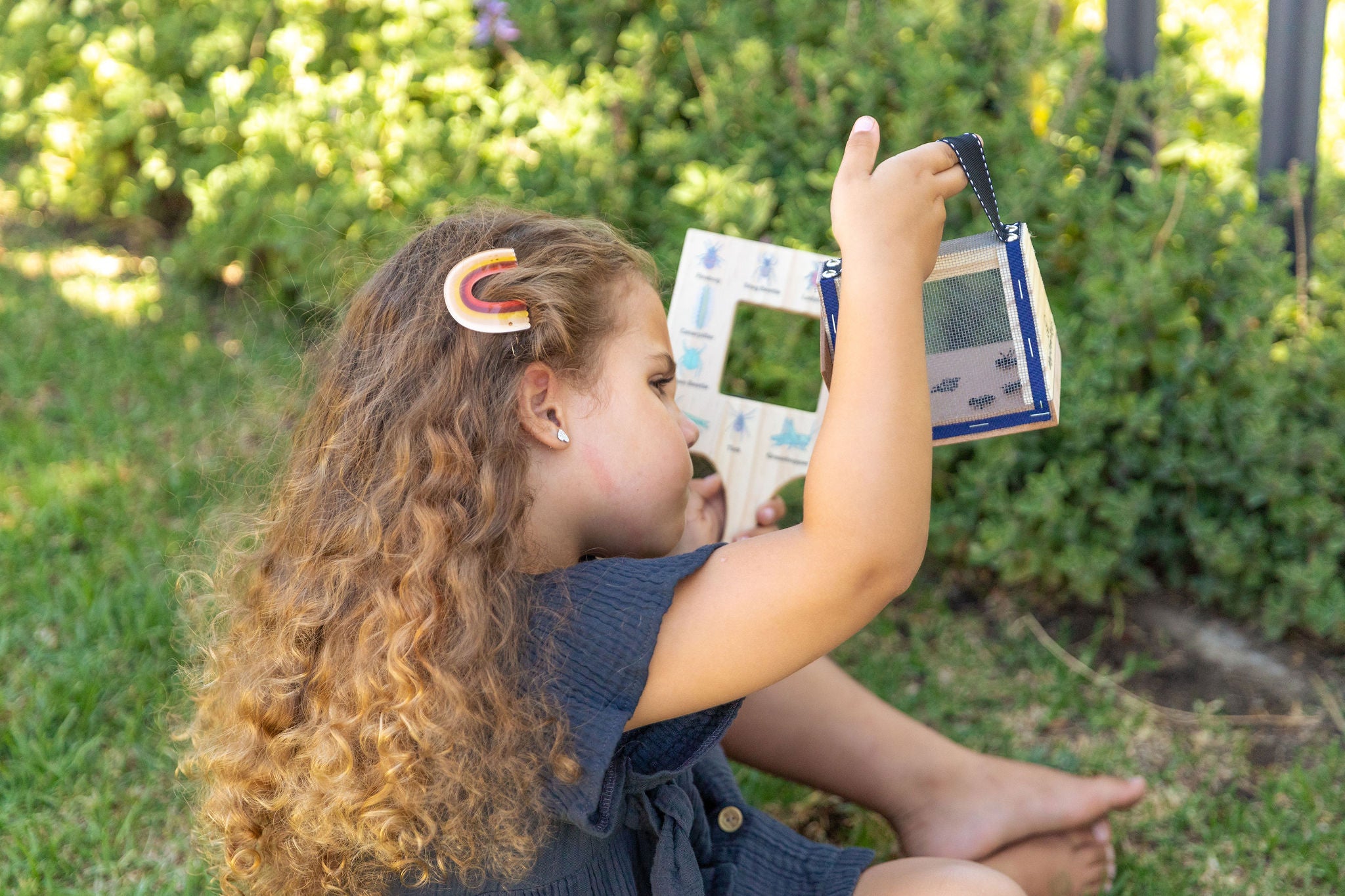 Child using wooden gogga box to collect and observe insects outdoors - nature play and science exploration toy
